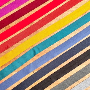 May include: A collection of colorful elastic bands in various shades of pink, purple, red, orange, yellow, teal, blue, navy, gray, and black. The bands are arranged diagonally on a wooden surface.