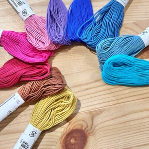 May include: A collection of 10 spools of embroidery floss in various colors, including pink, red, orange, yellow, blue, and green. Each spool is labeled with the color number and the brand name "Olympus".