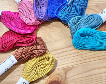 May include: A collection of 10 spools of embroidery floss in various colours, including pink, red, orange, yellow, blue, and green. Each spool is labelled with the colour number and the brand name "Olympus".