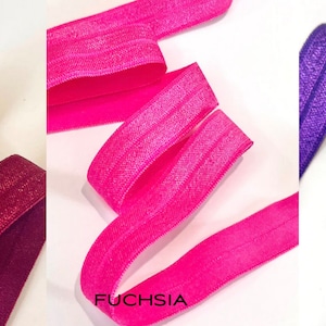 Puede incluir: Tres rollos de cinta el&aacute;stica en colores vino, fucsia y morado. Cada rollo tiene un brillo sutil y un patr&oacute;n texturizado.