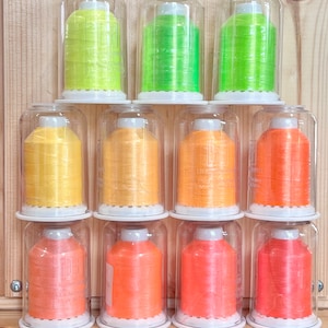 May include: Ten spools of thread in clear plastic containers. The spools are arranged in three rows. The top row has three spools of green thread. The middle row has four spools of yellow thread. The bottom row has three spools of orange thread.