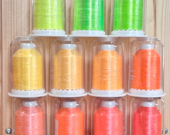 May include: Ten spools of thread in clear plastic containers. The spools are arranged in three rows. The top row has three spools of green thread. The middle row has four spools of yellow thread. The bottom row has three spools of orange thread.