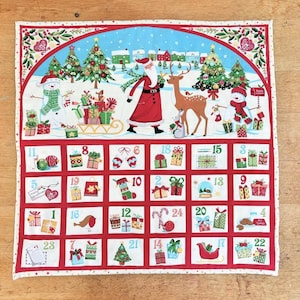 May include: A festive Christmas advent calendar. The top section depicts a winter scene with Santa, a reindeer, and snowmen. The calendar has 24 numbered pockets, each with a different Christmas-themed illustration.