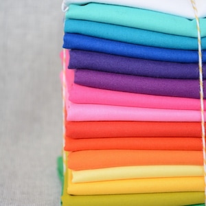 Könnte beinhalten: Ein Stapel farbiger Stoffquadrate in Regenbogenfarben, darunter Weiß, Türkis, Blau, Lila, Rosa, Orange, Gelb und Grün. Der Stoff ist ordentlich gefaltet und mit einer Schnur gebunden, ideal für Bastel- und Nähprojekte, jedes Quadrat misst etwa 20 cm.