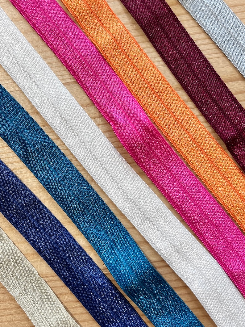 Puede incluir: Surtido de ocho gomas el&aacute;sticas para el cabello de colores con un acabado brillante. Las gomas para el cabello est&aacute;n dispuestas en una fila sobre una superficie de madera. Los colores incluyen plata, blanco, azul verdoso, azul marino, rosa, naranja, burdeos y plata.