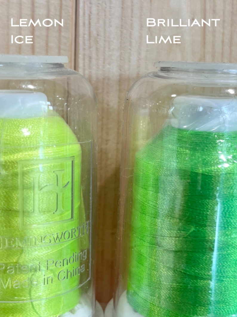 May include: Two spools of thread in clear plastic containers. The spool on the left is a bright yellow-green colour and labelled "Lemon Ice". The spool on the right is a bright green colour and labelled "Brilliant Lime". Both spools are labelled "DMC" and "Patent Pending Made in China."