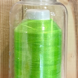 May include: A spool of neon green thread in a clear plastic container. The container has a white lid and a white base with holes.