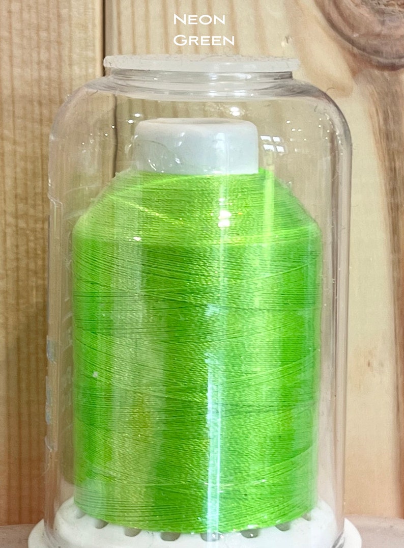 May include: A spool of neon green thread in a clear plastic container. The container has a white lid and a white base with holes.