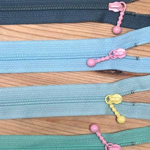May include: Four zipper pulls with different colored plastic sliders. The zippers are in four colors: dark gray, light blue, a lighter shade of blue, and green.