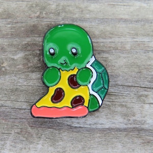 May include: A green turtle with a cute face is holding a slice of pizza with red pepperoni. The turtle is wearing a green and white shell with a black outline.