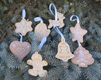 May include: Eight gingerbread ornaments with white embroidery designs hanging on a blue spruce tree. The ornaments include a snowflake, mitten, heart, reindeer, star, bell, tree, and gingerbread person.