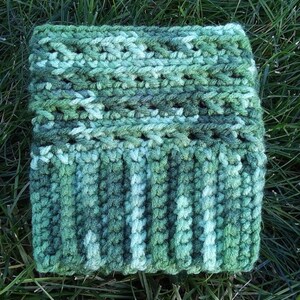 May include: A green and white crocheted cowl with a textured pattern. The cowl is made with a variegated yarn that creates a subtle ombre effect.