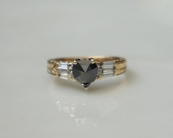 Pode incluir: Um anel de ouro com um diamante preto em forma de coração e dois diamantes menores de cada lado.