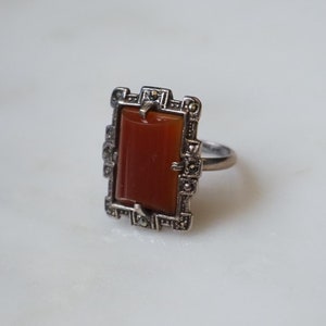 May include: A silver ring with a rectangular carnelian stone set in a geometric frame of marcasite.