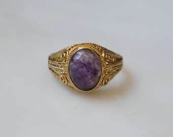 May include: A gold ring with an oval-shaped purple gemstone set in a detailed ornate design.