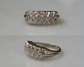 Pode incluir: Um anel de prata com uma fileira de pequenos diamantes engastados em uma banda retangular.