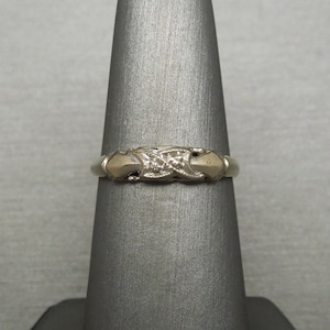 May include: A gold band ring with a diamond set in a delicate, intricate design. The ring is on a gray ring display stand.