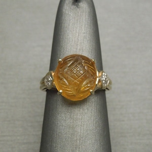 May include: A gold ring with a carved orange gemstone and two small diamonds on the sides.