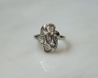 Op de afbeelding: Een zilveren ring met een delicaat, versierd ontwerp met een bloemenmotief en drie kleine diamanten.