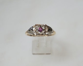 May include: A gold ring with a square-shaped ruby gemstone surrounded by smaller diamonds. The ring has a delicate design with intricate details.
