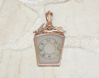 May include: A gold-toned pendant with a white, circular, faceted stone. The stone has a ring of numbers around it, and the pendant has a decorative design at the top.