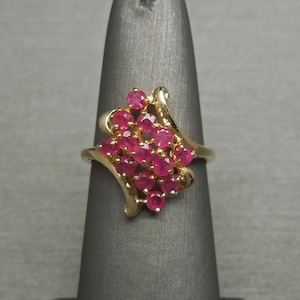 May include: A gold ring with a cluster of pink ruby stones set in a swirling design.