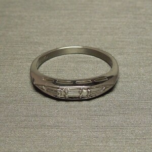 May include: A silver band ring with a row of small, rectangular-shaped diamonds set in the center.