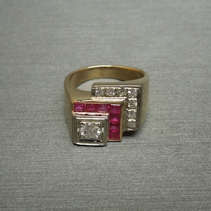 May include: A gold ring with a large square diamond and smaller ruby stones set in a geometric design.
