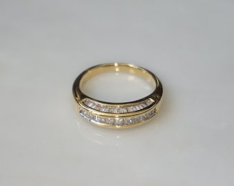 Pode incluir: Um anel de banda de ouro com uma fileira de pequenos diamantes de forma baguette transparentes.