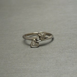 May include: A silver ring with two heart-shaped designs, each with a small diamond in the center.