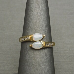 K&ouml;nnte beinhalten: Ein goldener Ring mit zwei birnenf&ouml;rmigen Opalen und einer Reihe kleiner Diamanten auf jeder Seite.
