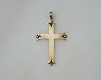 May include: A gold-colored cross pendant with a simple design. The cross has a loop at the top for a chain and decorative elements at the ends of each arm. The pendant is displayed against a white background.