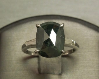 May include: A silver ring with a large, dark green, cushion-cut gemstone surrounded by two smaller, clear gemstones.