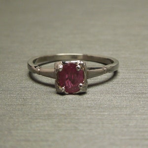 May include: A silver ring with a pink oval gemstone set in a prong setting.