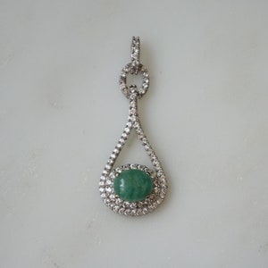 May include: A silver pendant with a teardrop-shaped design. The pendant features a green gemstone surrounded by clear stones.