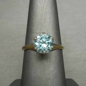 May include: A gold ring with a large, round, light blue gemstone set in a prong setting.