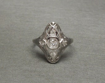 Op de afbeelding: Een zilveren ring met een diamantvormige zetting met een centrale diamant en kleinere diamanten eromheen.