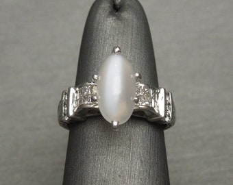 May include: A silver ring with a white oval gemstone surrounded by smaller white gemstones.