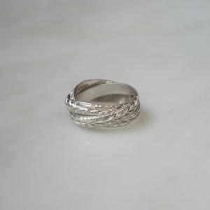 May include: A silver ring with a woven design. The ring is made of a shiny, metallic material and features a detailed pattern. The ring is a piece of jewelry, likely for everyday wear or special occasions.