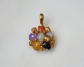 Puede incluir: Un colgante de oro con un diseño de flor que presenta siete piedras preciosas ovaladas de varios colores, incluyendo morado, verde, blanco, naranja, amarillo y negro.