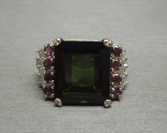 May include: A silver ring with a large, dark green emerald-cut gemstone surrounded by smaller pink and white gemstones.