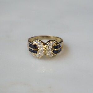 May include: A gold ring with a double-sided design featuring a row of blue sapphires and a cluster of white diamonds.