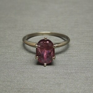 May include: A silver ring with a pink oval gemstone set in a prong setting.
