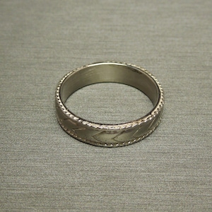May include: A silver ring with a patterned design. The ring is smooth and shiny.