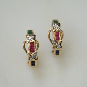 May include: A pair of gold hoop earrings with a design of alternating red, green, and blue gemstones set in a gold and white metal setting.