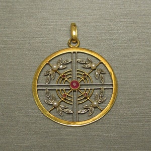 May include: A gold pendant with a circular design featuring a central ruby surrounded by smaller rubies and pearls. The pendant is set in a geometric pattern with delicate leaves and a cross-shaped design.