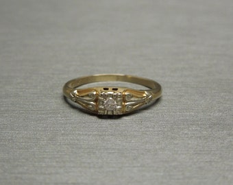 May include: A gold ring with a small diamond set in a square-shaped setting. The ring has a delicate design with intricate details.