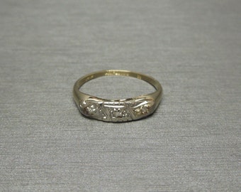 May include: A gold band ring with three small diamonds set in a decorative design.