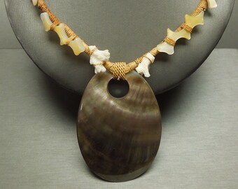May include: A brown and white shell necklace with a large, oval-shaped shell pendant. The necklace is made of braided cord and features small, white shell beads.
