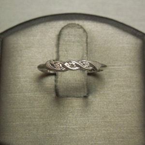 May include: A silver band ring with three small diamonds set in a twisted design.
